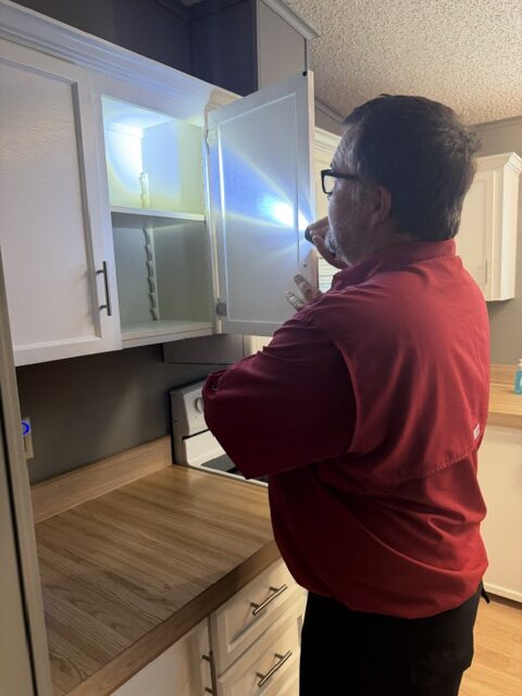 Haynes technician inspecting inside a kitchen cabinet with a flashlight